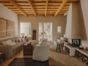 Living room at Bos-Cos Menorca with exposed ceiling beams, fireplace, striped sofa, wooden furniture, and courtyard views.