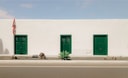 White street facade with green doors and minimal landscaping at Casa Montelogo.